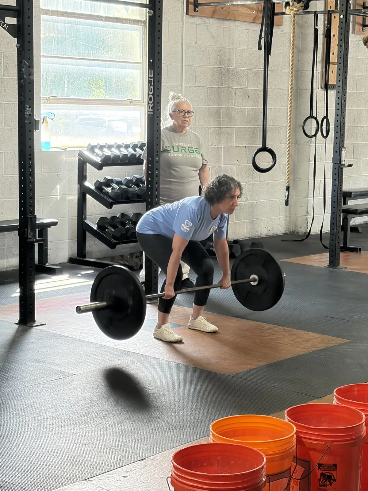 A Senior Fitness member setting up a barbell deadlift while a classmate looks on