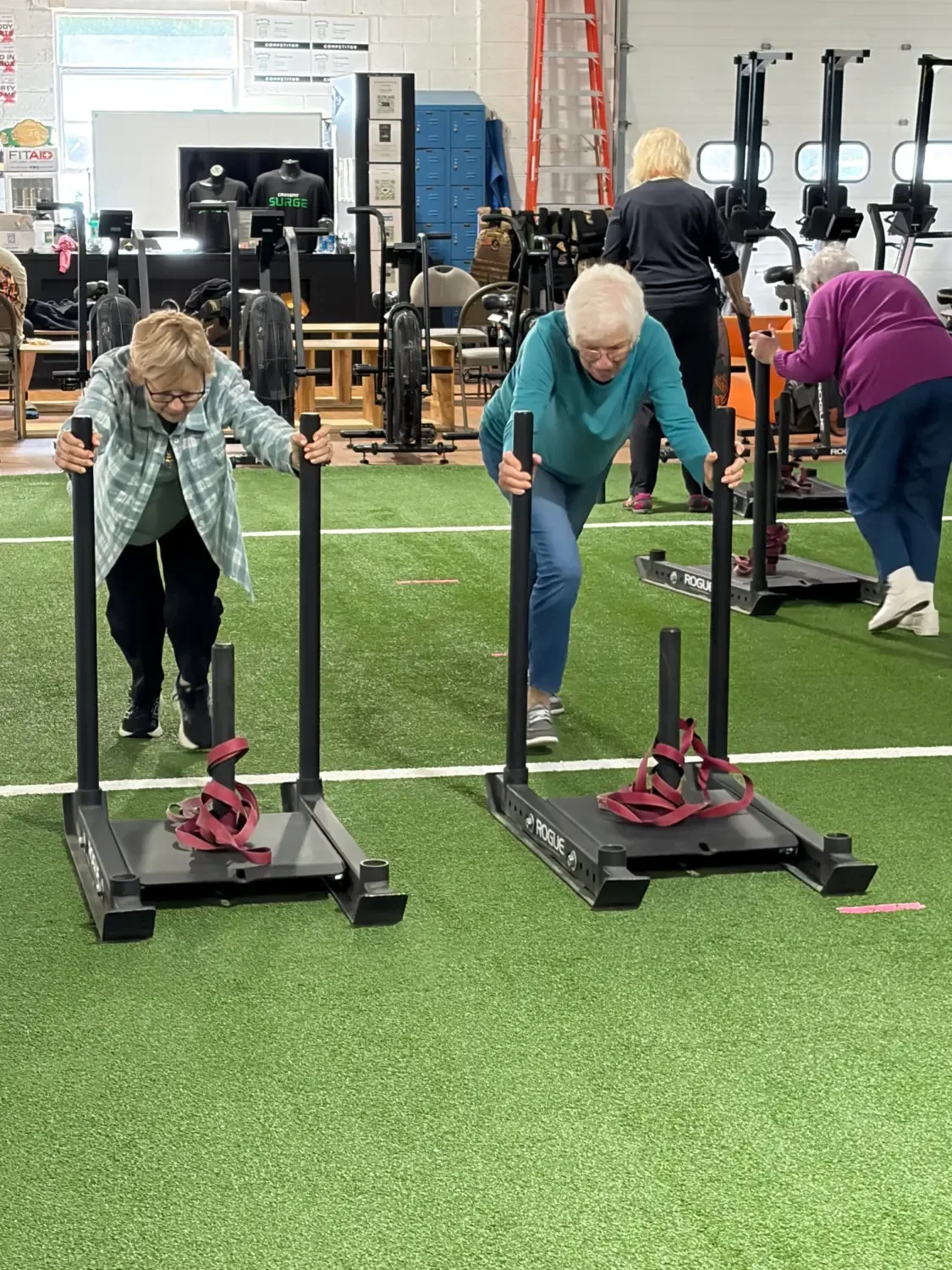 Senior Fitness members pushing sleds on the turf